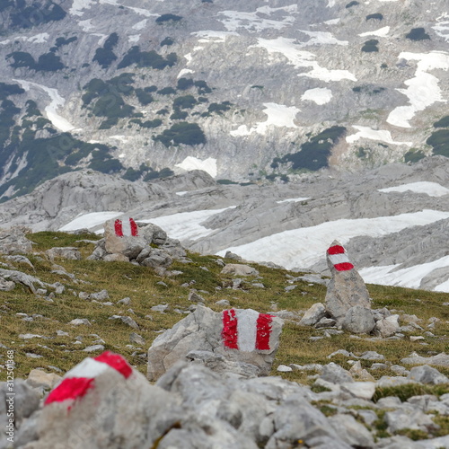 Red hiking marks painted on stones in grass with snow and high rocky mountains in the background, Alps, Austria. photo