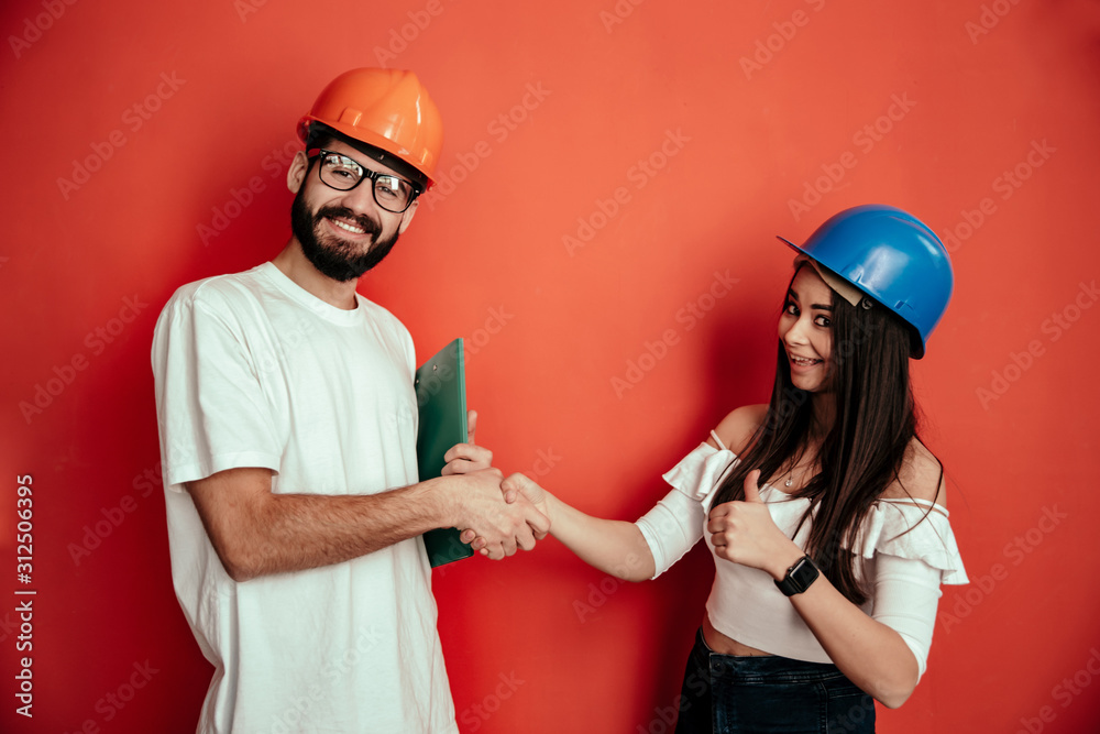 Two mid adults constructors workers giving hand shake isolated on red background Two mid adults constructors workers giving hand shake isolated on red background