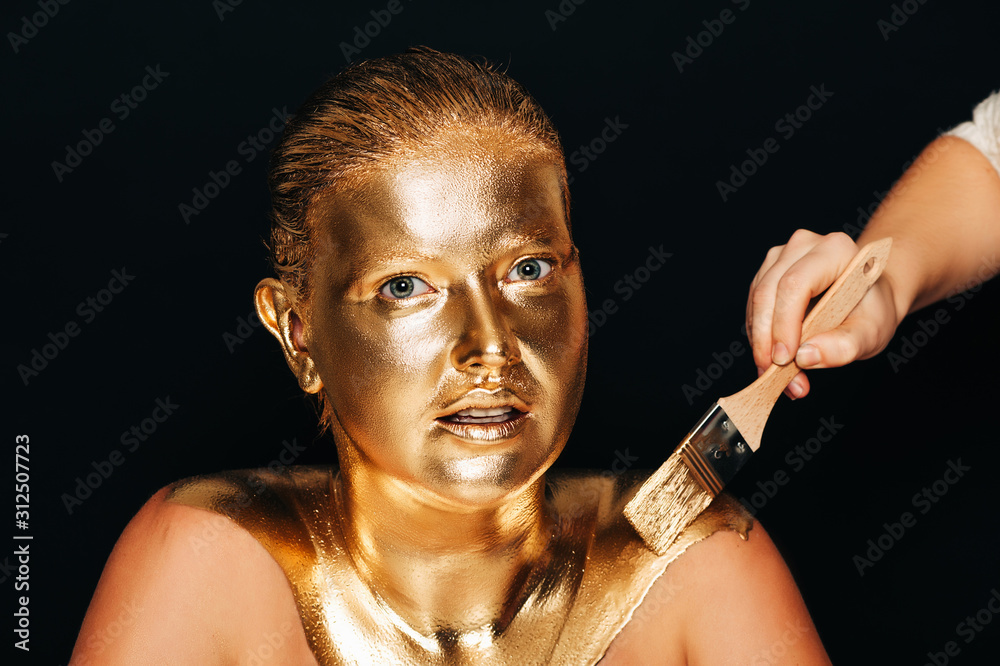 Artist painting beautiful young model in gold color paint, body