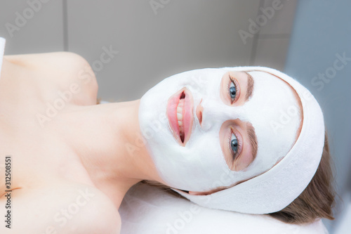 beautiful young woman with a cosmetic mask on her face lies in a beauty salon. Beautiful smile, blue eyes