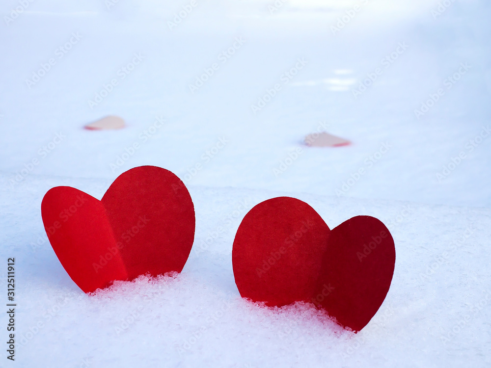 Fototapeta premium Red paper hearts on white snow as a symbol of love and warmth.