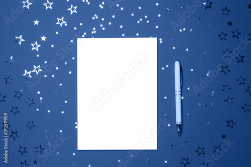 Notebook with pen for writing on trendy blue background of star-shaped confetti. Festive and celebration concept. Main color trend of the year 2020.