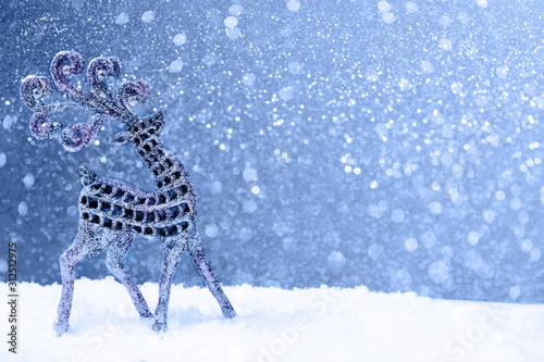 Silver beautiful glitter deer walking under the falling snow on blue holiday and anf festive background with copy space for text. Marry Christmas and Happy New Year concept.