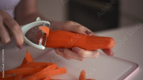 Hands of a young girl rub an orange carrot using a grater. Preparing fresh carrots before cooking on kitchen.