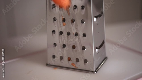 Hands of a young girl rub an orange carrot using a grater. Preparing fresh carrots before cooking on kitchen.