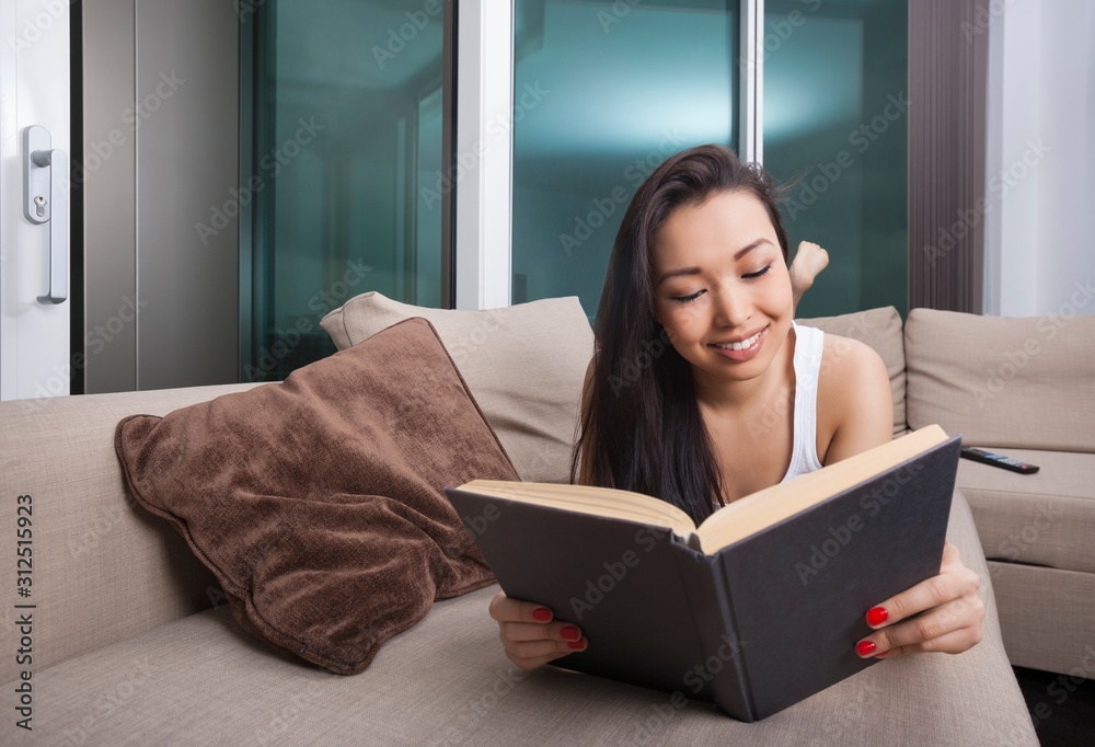 Happy young woman reading book while lying on sofa Happy young woman reading book while lying on sofa