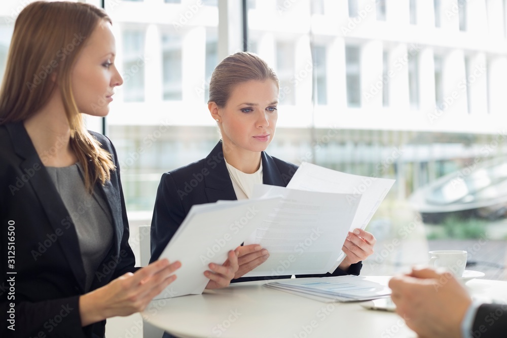 Businesswomen discussing over documents in office cafeteria Businesswomen discussing over documents in office cafeteria