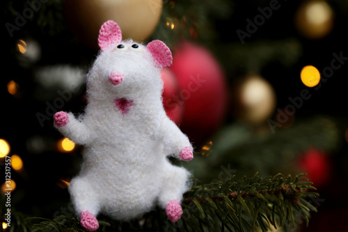 New Year card with white knitted toy rat on background of fir branches and golden lights. Chinese Year of Rat, Zodiac symbol 2020
