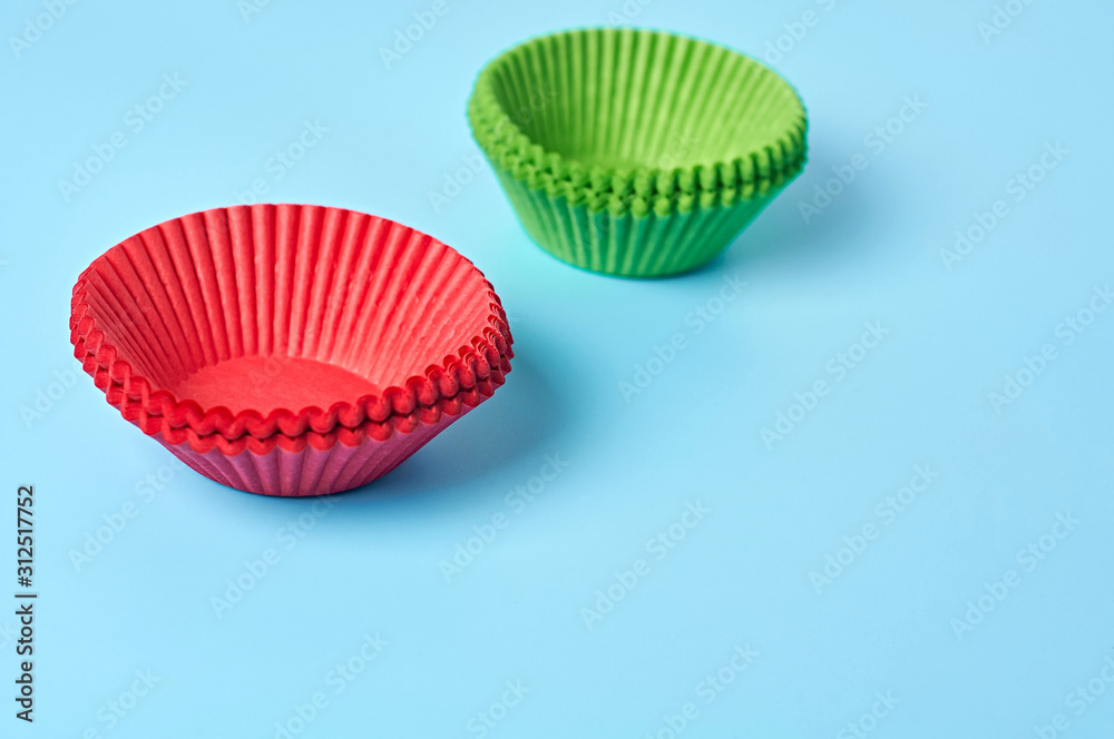 Two heaps of new red and green paper molds for baking muffins lies on blue desk on kitchen. Space for text