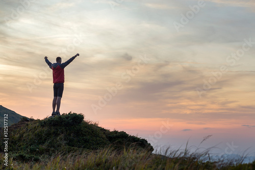 Dark silhouette of a hiker climbing a mountain at sunset raising his hands standing on summit like a winner.