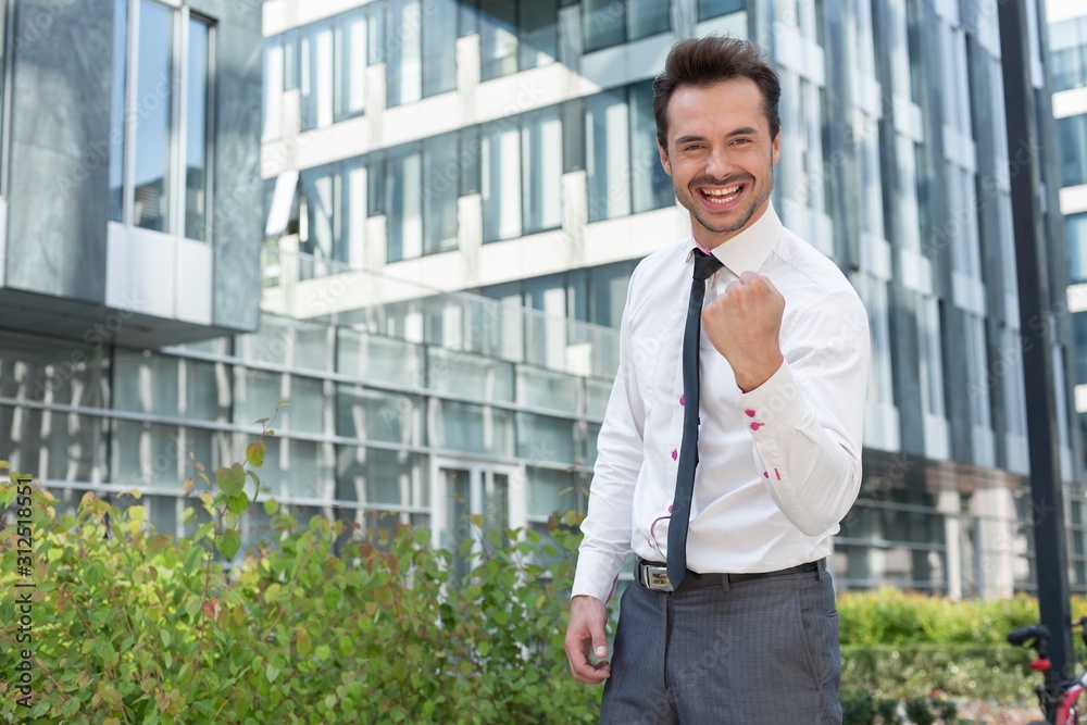 Portrait of happy businessman with clenched fist standing outside office building Portrait of happy businessman with clenched fist standing outside office building