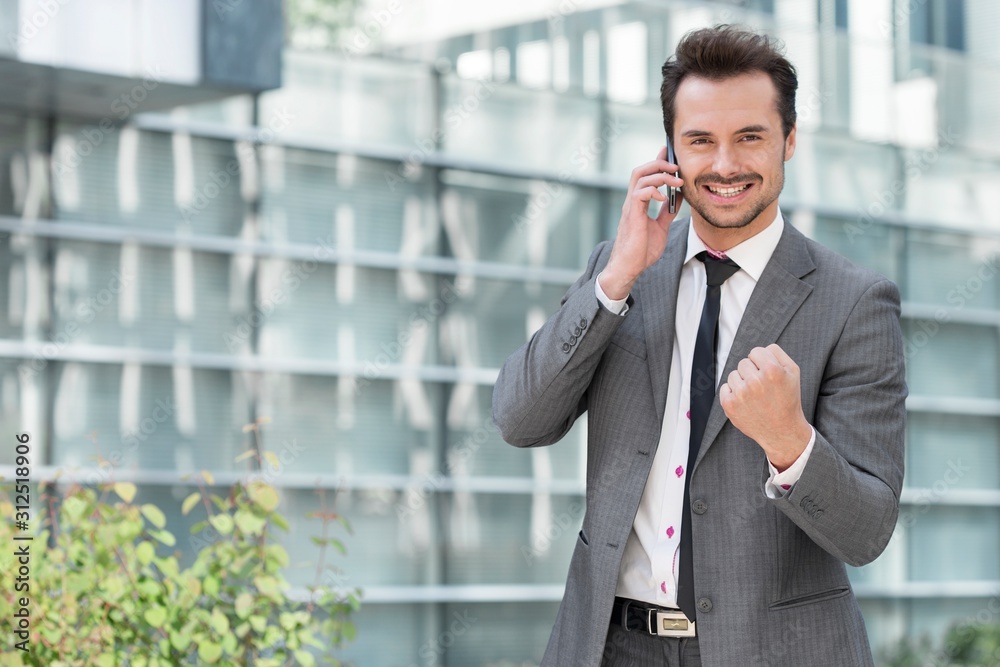 Portrait of successful young businessman using cell phone against office building Portrait of successful young businessman using cell phone against office building