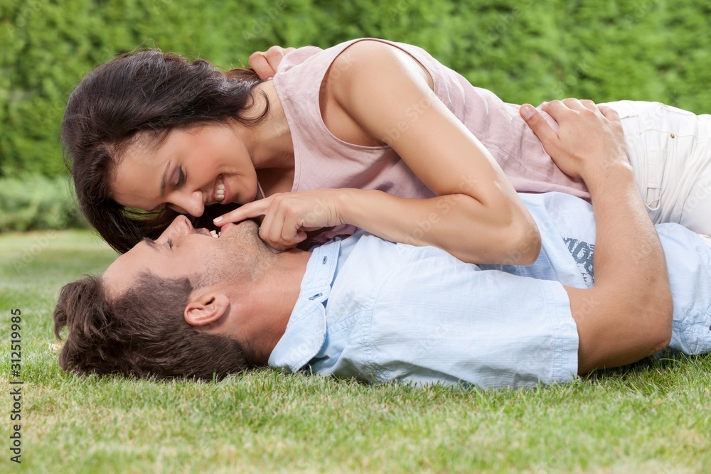 Romantic young woman touching man's lips while lying on him in park Romantic young woman touching man's lips while lying on him in park