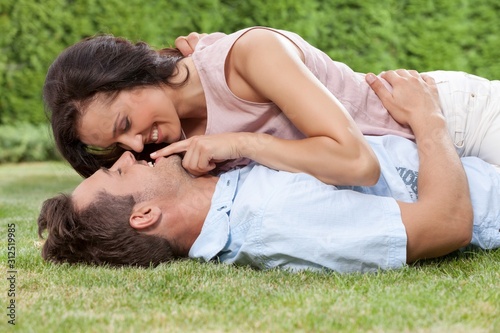 Romantic young woman touching man's lips while lying on him in park
