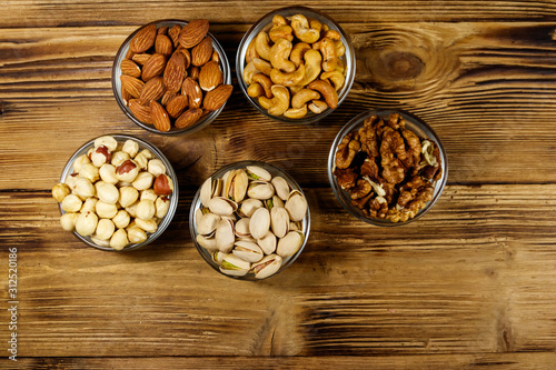 Assortment of nuts on wooden table. Almond, hazelnut, pistachio, walnut and cashew in glass bowls. Top view. Healthy eating concept