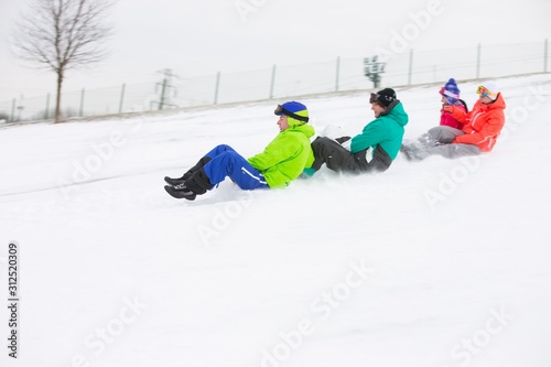 Canvas Print Side view of young friends sledging on snow covered slope
