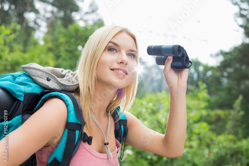 Young female hiker using binoculars in forest