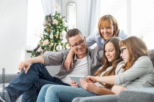 Family using tablet PC on sofa with Christmas tree in background