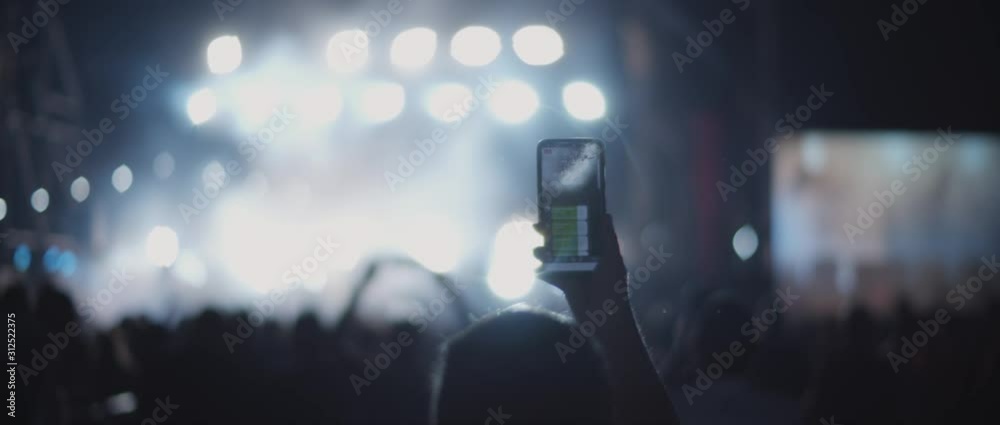 Person taking a picture during a concert, with floodlights flashing in ...