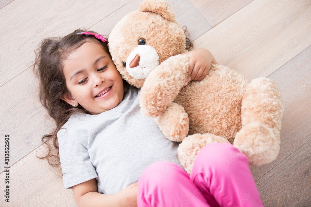 Girl with teddy bear lying on wooden floor at home
