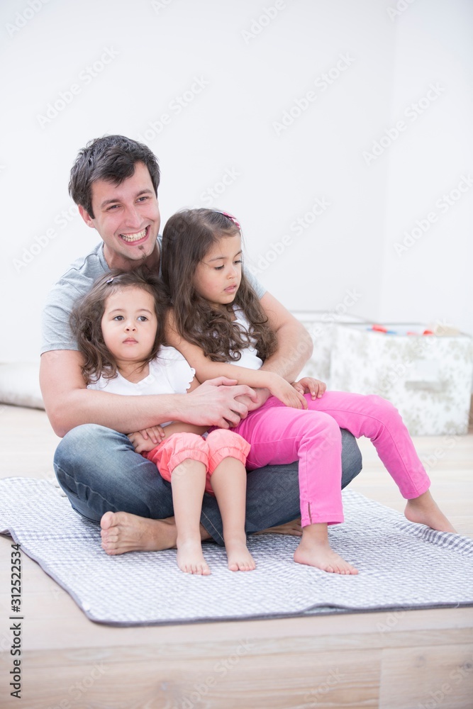 Smiling young man with daughters sitting in his lap at home Smiling young man with daughters sitting in his lap at home