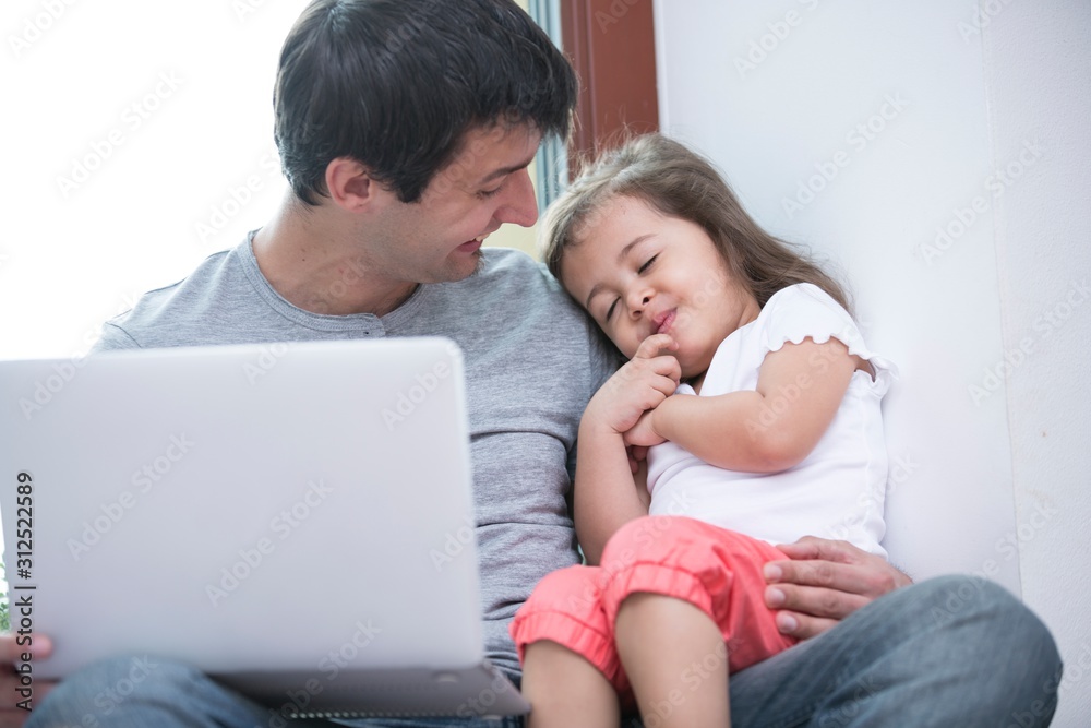 Happy father looking at cute daughter sleeping while using laptop at home Happy father looking at cute daughter sleeping while using laptop at home