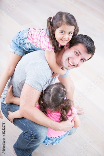 High angle portrait of playful father carrying girls at home