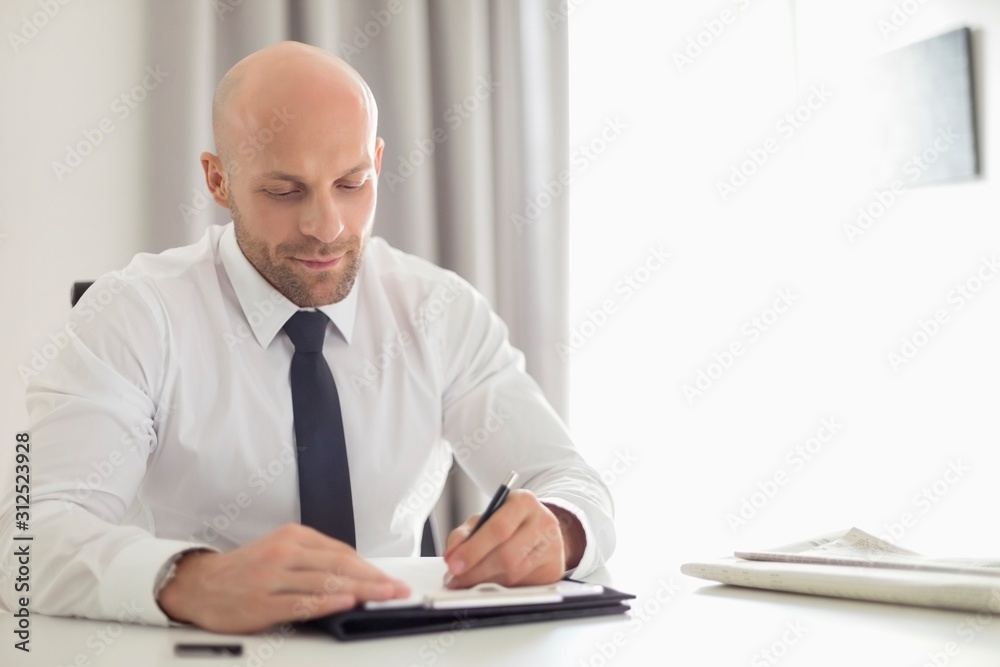 Mid adult businessman writing on clipboard in home office Mid adult businessman writing on clipboard in home office