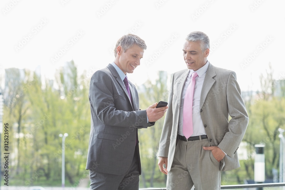 Businessmen using cell phone together outdoors Businessmen using cell phone together outdoors
