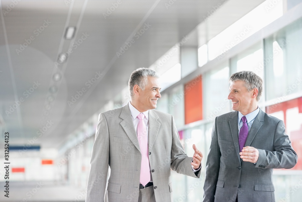 Happy middle aged businessmen talking while walking in railroad station Happy middle aged businessmen talking while walking in railroad station