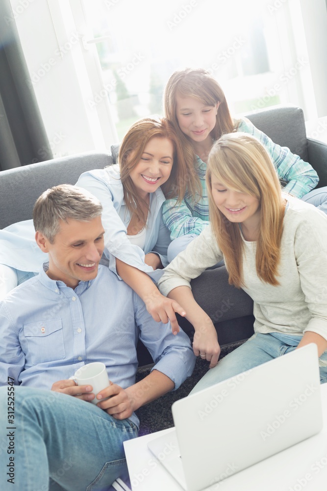 Happy parents with daughters using laptop in living room