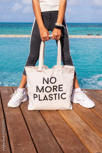 Young girl holding cotton eco bag with sign No More Plastic on blue tropical sea background