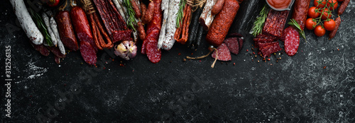 Background of salami, sausages and meat products, on black stone background. Top view. Free space for your text.