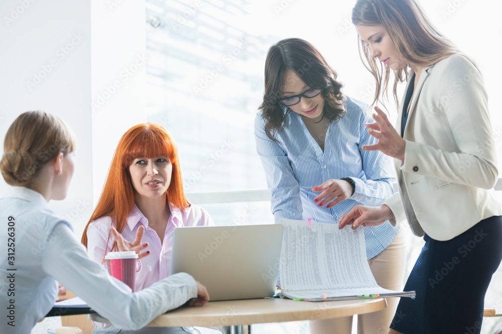 Businesswomen discussing over documents at table in office Businesswomen discussing over documents at table in office
