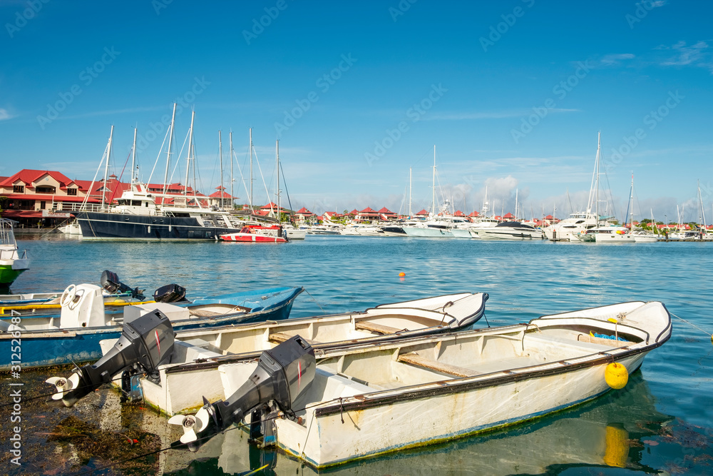 Fototapeta premium Simple old fishing boats and Luxury yachts and Boats in background in sunny summer day at marina of Eden Island, Mahe, Seychelles