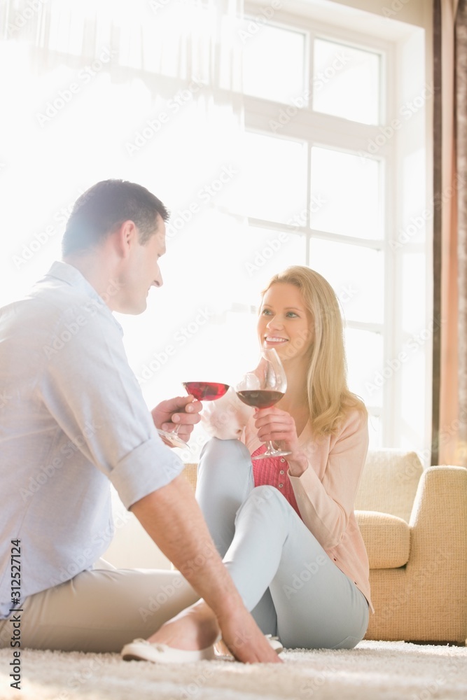 Happy couple looking at each other while having red wine at home Happy couple looking at each other while having red wine at home
