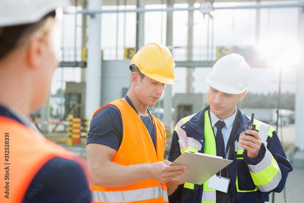 Workers discussing over clipboard in shipping yard Workers discussing over clipboard in shipping yard