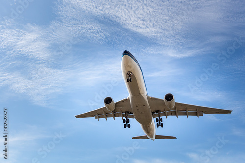 White and silver plane with chassis is landing on the blue sky with clouds background photo