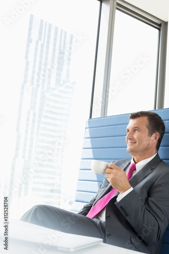 Happy mature businessman taking coffee break in office