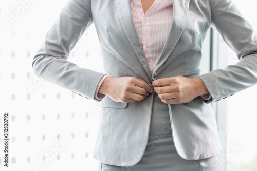 Midsection of businesswoman buttoning her blazer