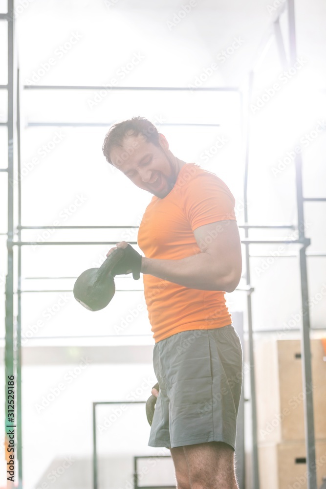 Confident man lifting kettlebell in crossfit gym