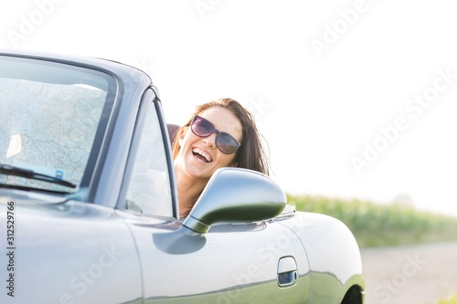 Excited woman enjoying road trip in convertible against clear sky