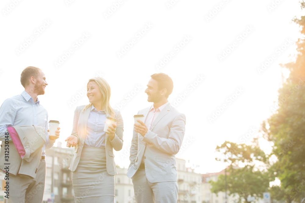 Happy businesspeople with disposable cups talking against clear sky on sunny day Happy businesspeople with disposable cups talking against clear sky on sunny day