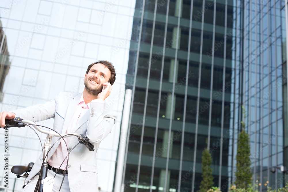 Low angle view of businessman answering mobile phone while sitting on bicycle outdoors Low angle view of businessman answering mobile phone while sitting on bicycle outdoors
