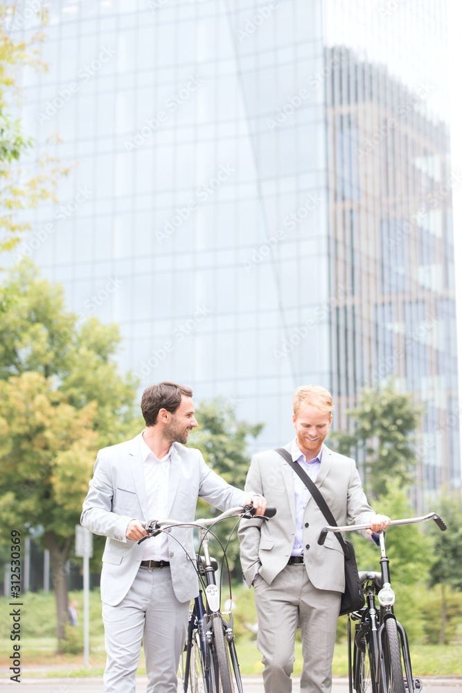 Φωτογραφία Businessmen with bicycles walking against office building