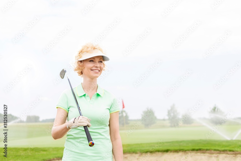 Happy middle-aged woman looking away while holding golf club Happy middle-aged woman looking away while holding golf club