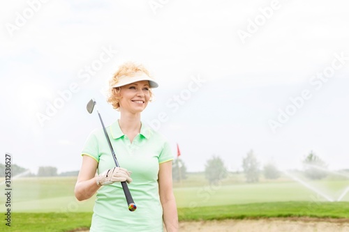 Happy middle-aged woman looking away while holding golf club