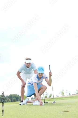 Man looking at woman aiming ball on golf course against sky