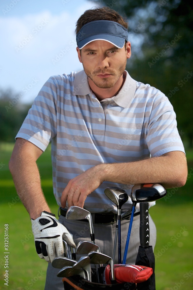 Portrait of young man standing by golf bag full of sticks