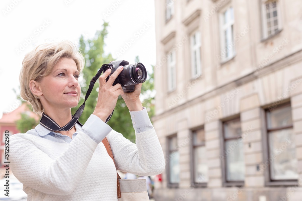 Middle-aged woman photographing through digital camera in city